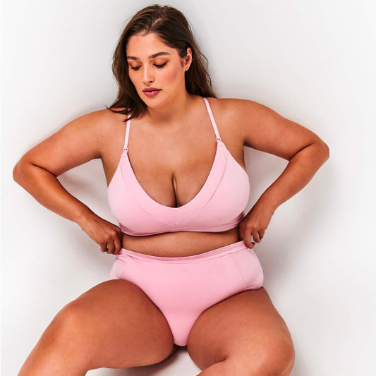 Model sits wearing the soft pink Maternity Bra and High Waisted Briefs