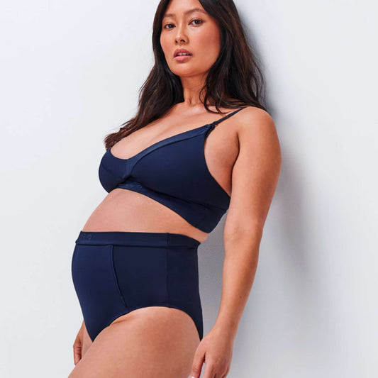 Campaign photo of model leaning against wall in NipCo navy Maternity Bra and High Waisted Briefs
