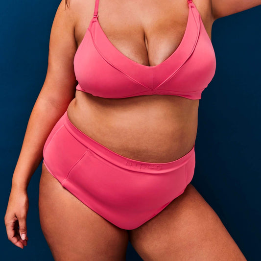 Model wears NipCo Maternity Bra and High Waisted Briefs in Coral against a navy background